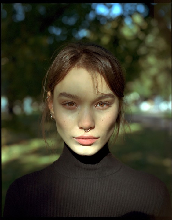 A woman with a nose ring and earrings is illuminated by dappled sunlight.