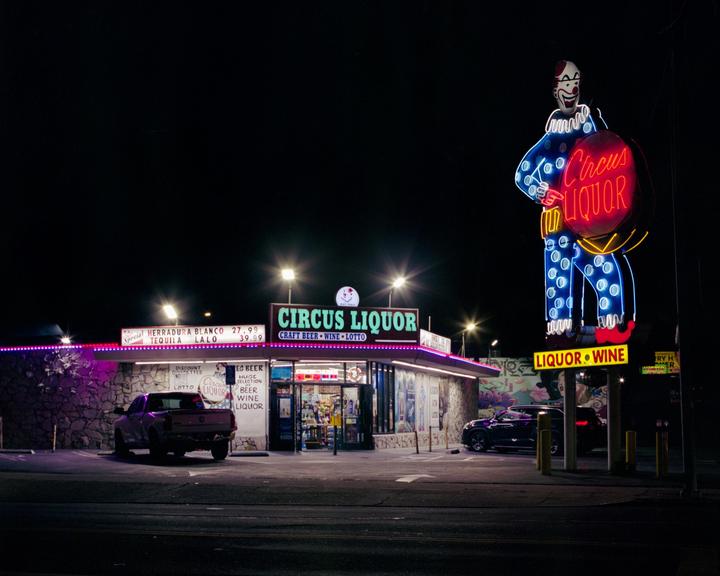 A liquor store with a large clown neon sign stands illuminated at night.