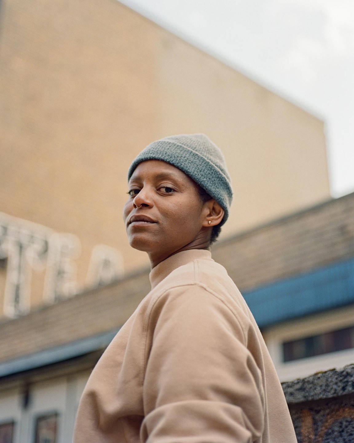 A woman wearing a beanie and a beige sweatshirt looks over her shoulder at the viewer.