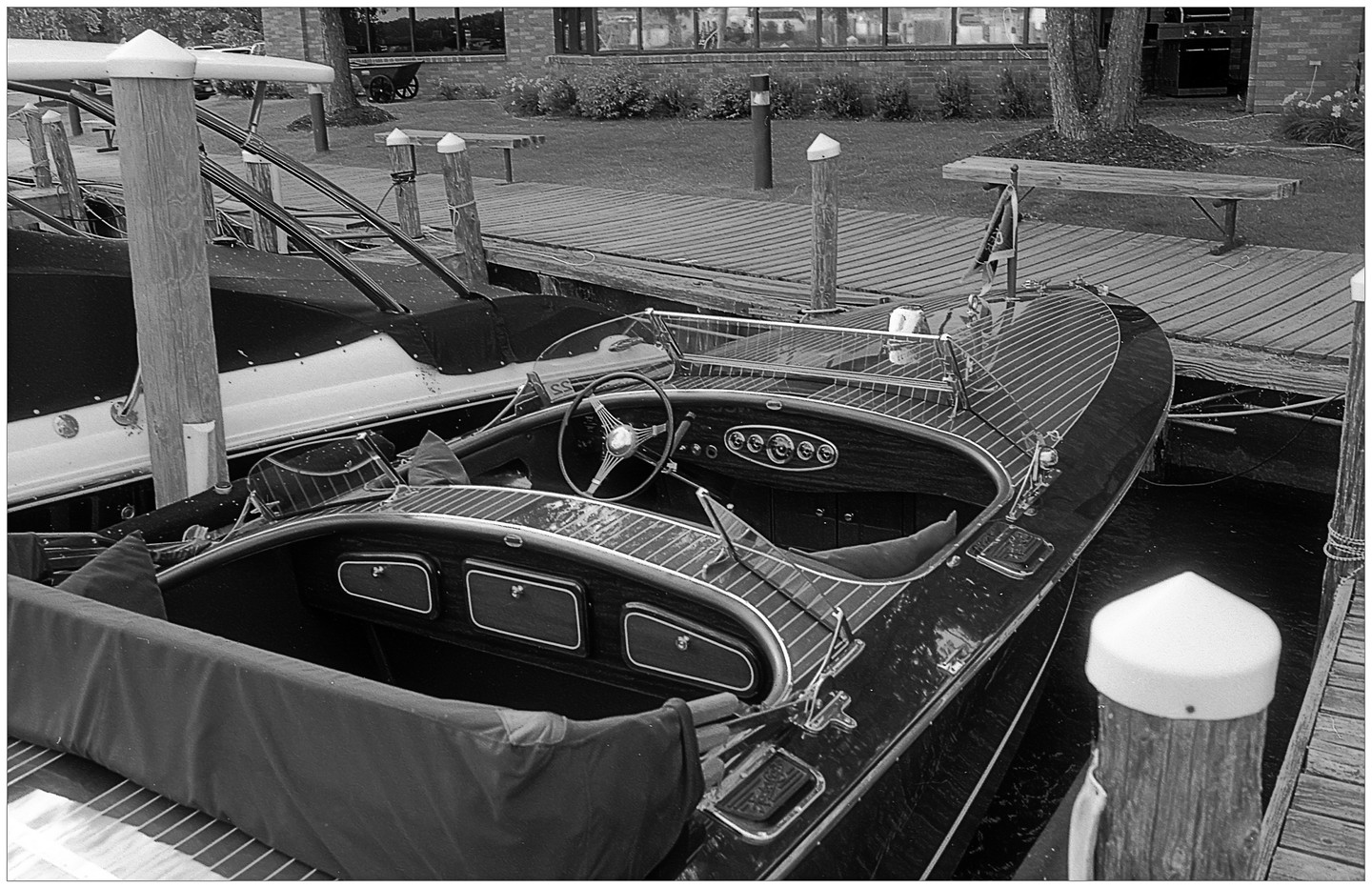 A wooden boat with a steering wheel is docked next to a pier.