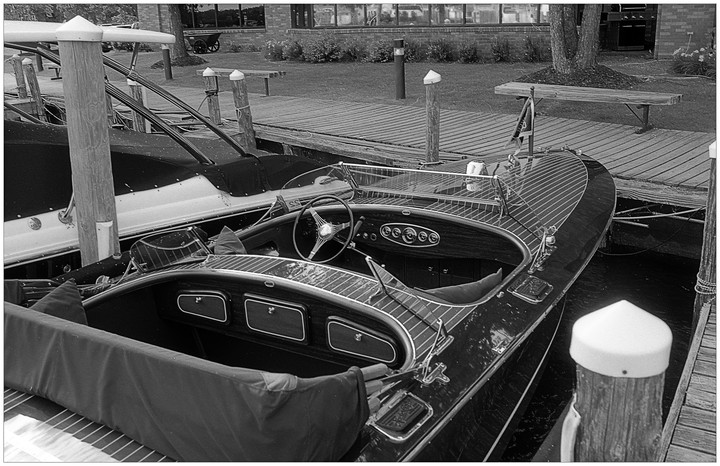 A wooden boat with a steering wheel is docked next to a pier.