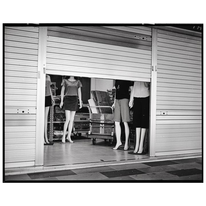 Several headless mannequins are visible behind a partially open metal roller shutter.