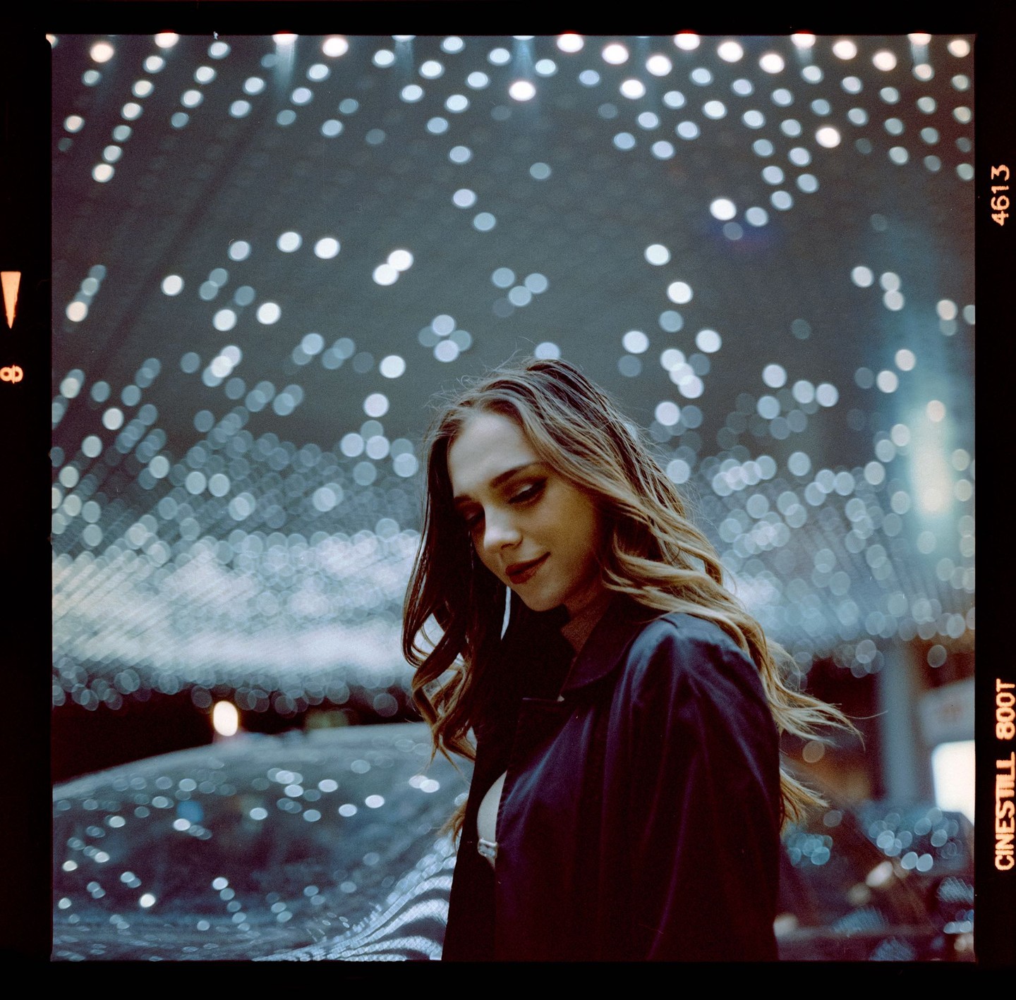 A woman with long wavy hair looks down, surrounded by many small, bright, out-of-focus lights.