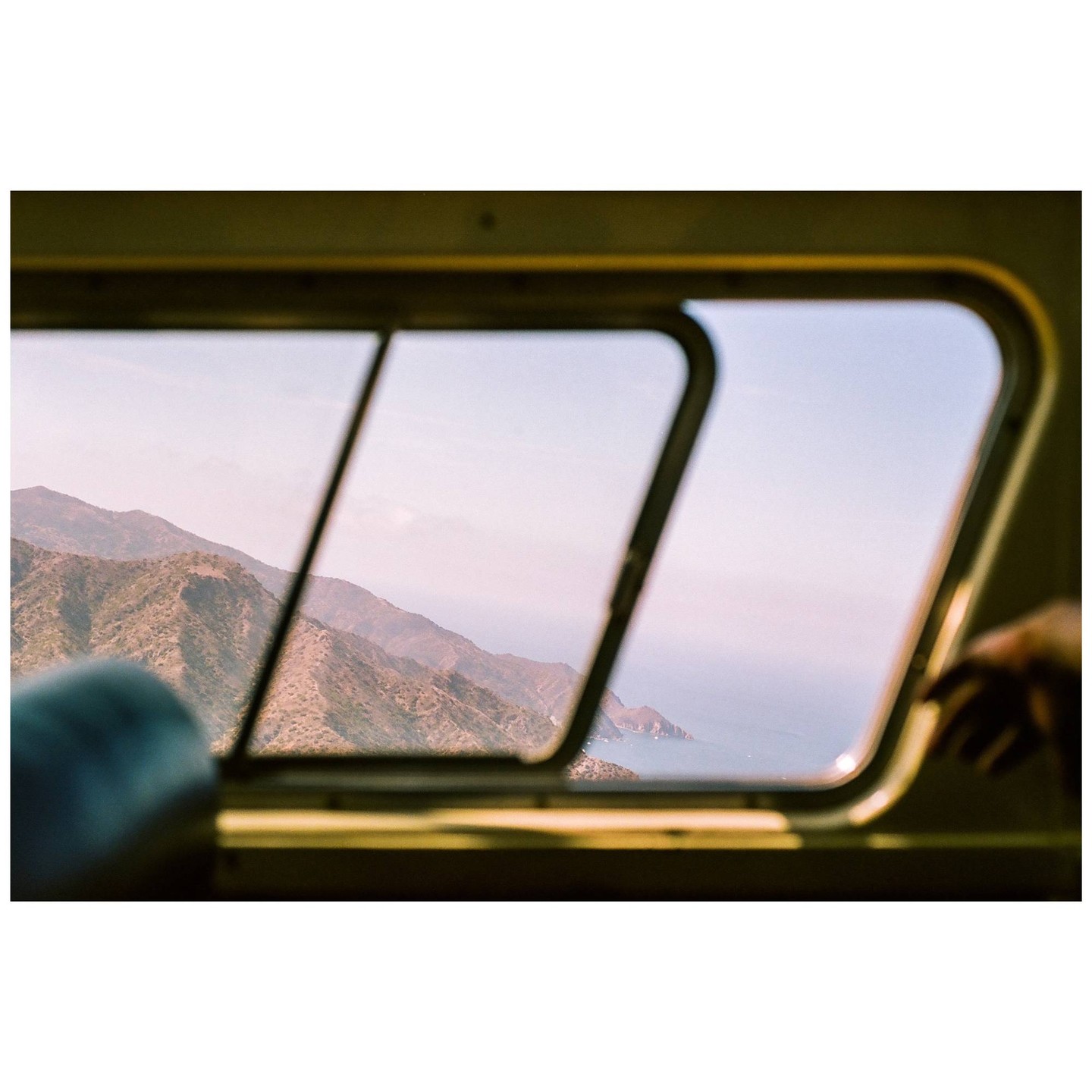 A view of mountains and ocean is seen through a window.