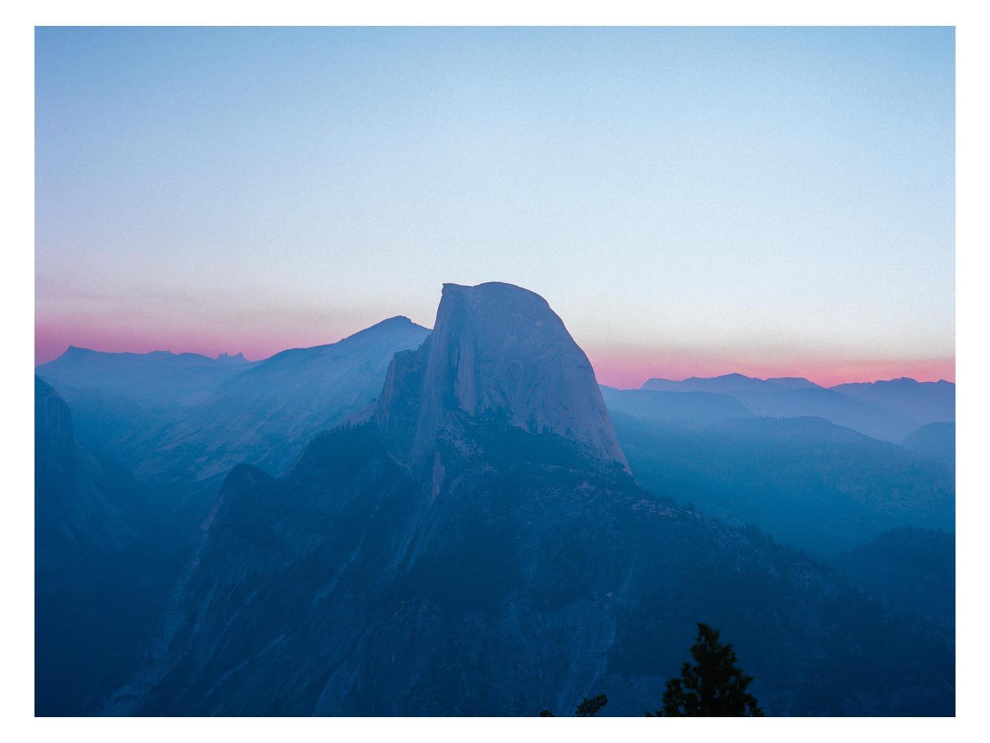 A sunrise over Half Dome shows a pink and blue sky above a mountain range.