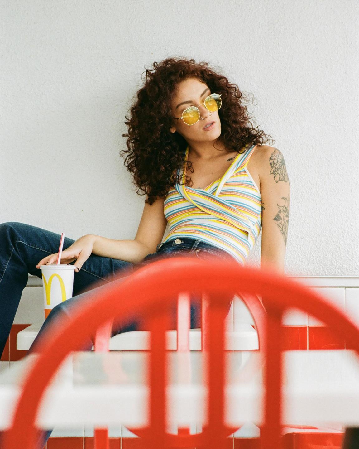 A woman with curly hair and yellow sunglasses sits with a McDonald's drink.