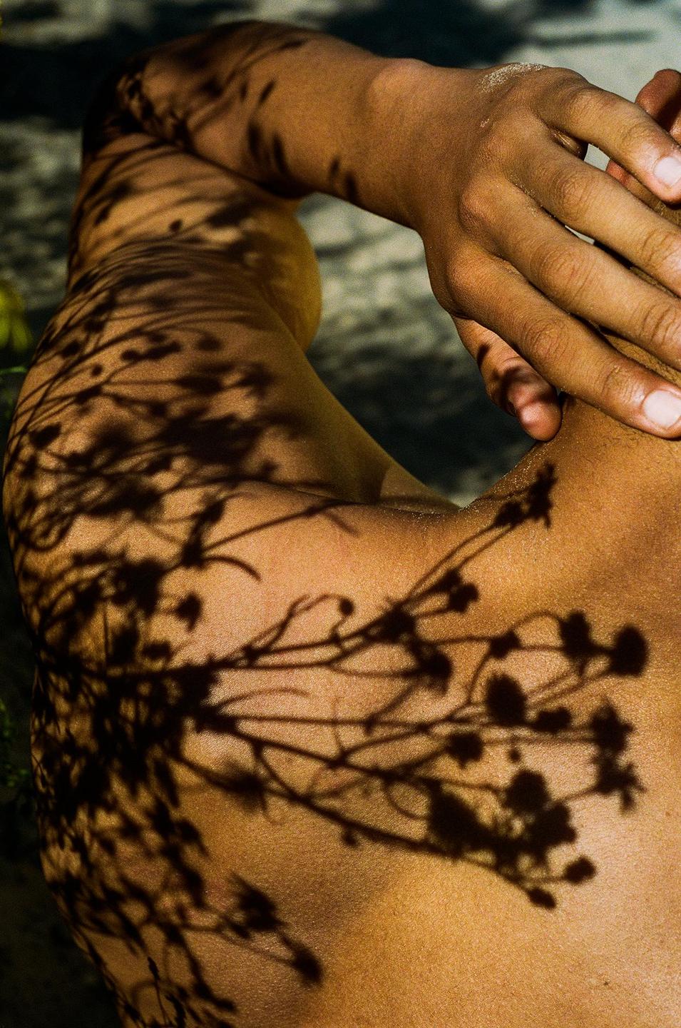 A person's arm and shoulder are covered in shadows from foliage.