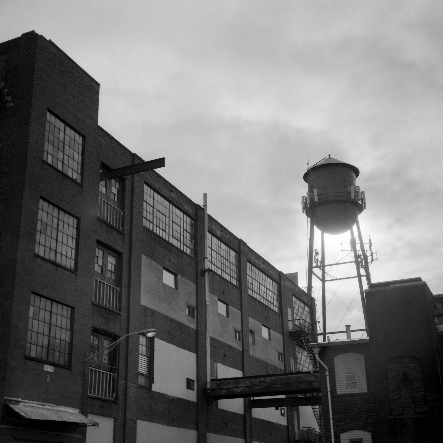 A water tower stands tall against a cloudy sky, next to a brick building with many windows.