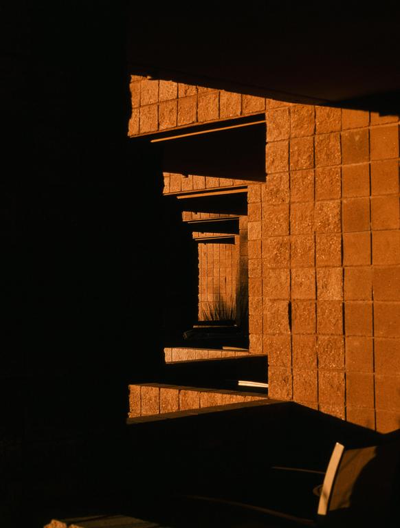 Sunlight illuminates a textured wall and a series of receding architectural elements, creating strong shadows.