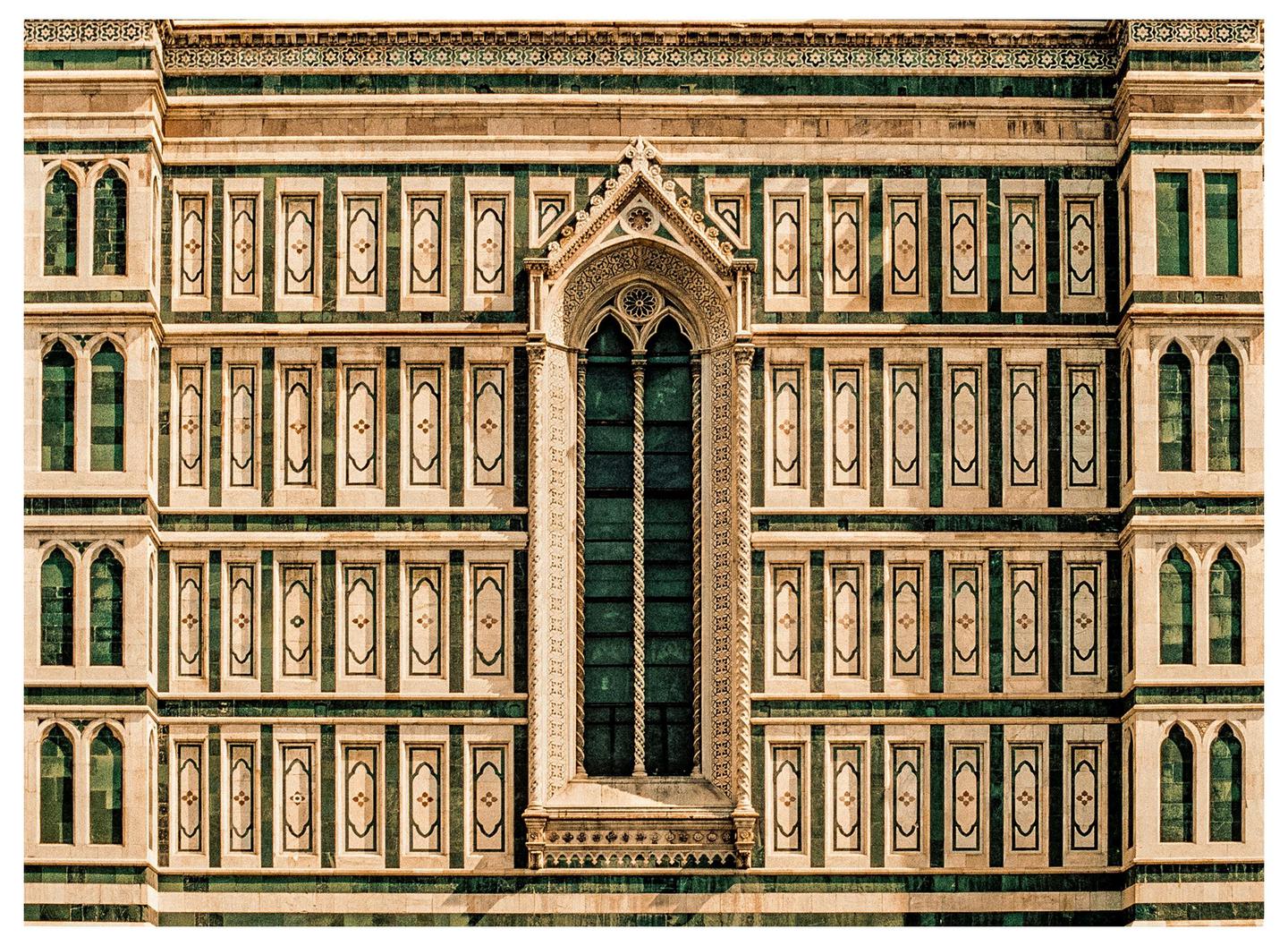 A large ornate window is centered on a building facade with many smaller windows and decorative panels.