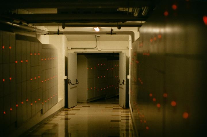 A long hallway with red lights on the walls leads to an open doorway.