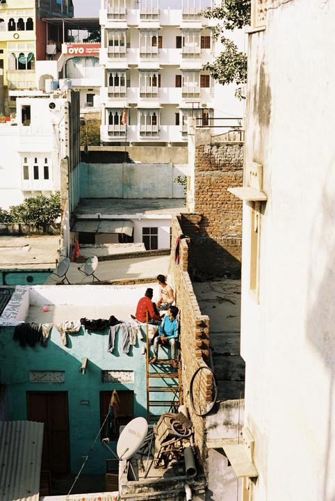 Three men sit on a rooftop in a city with many buildings.