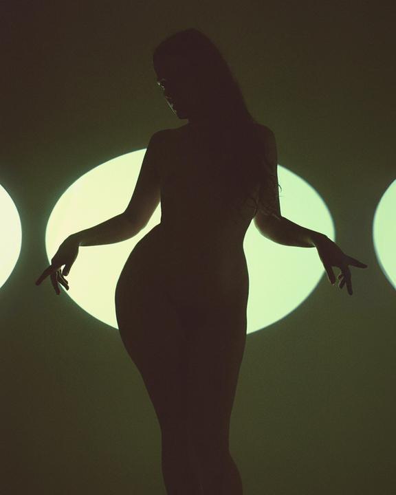 A woman is silhouetted against a wall with three bright circular lights.