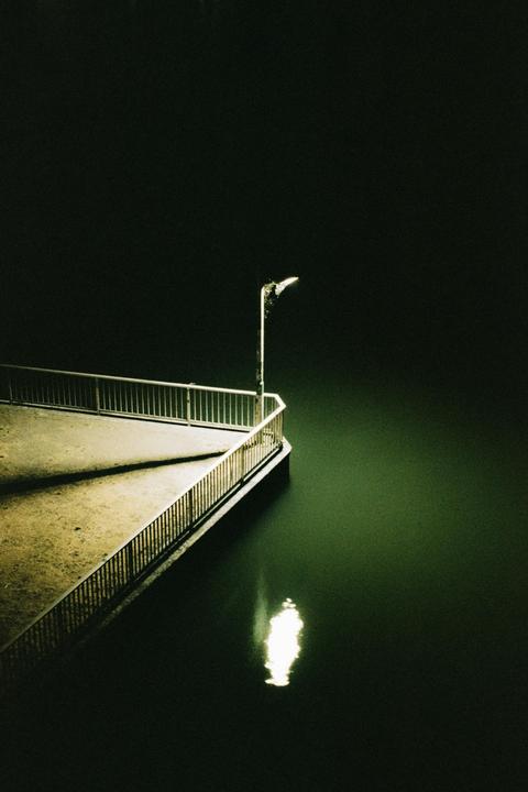 A street light illuminates a pier next to dark water at night.