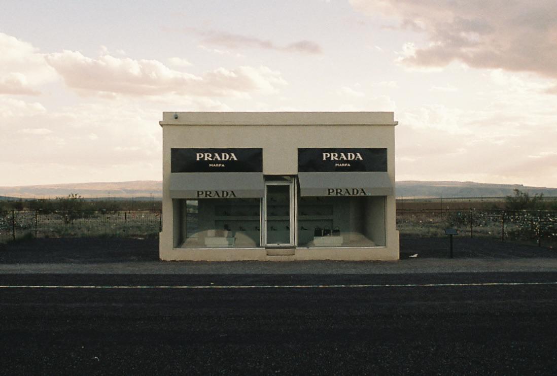 A Prada storefront stands alone on a flat landscape under a cloudy sky.