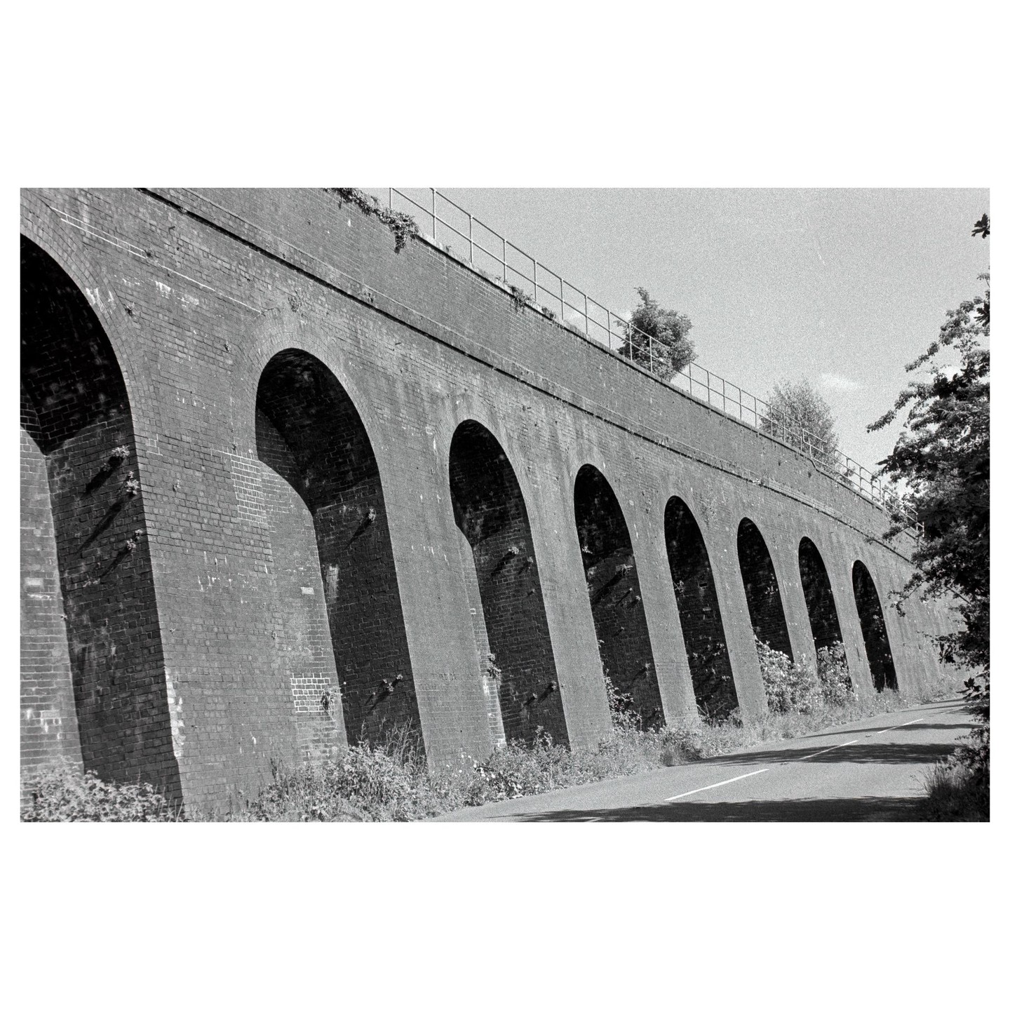 A long brick viaduct with many arches stretches across the frame next to a road.