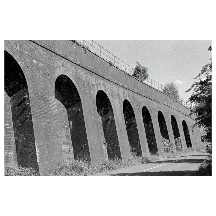 A long brick viaduct with many arches stretches across the frame next to a road.