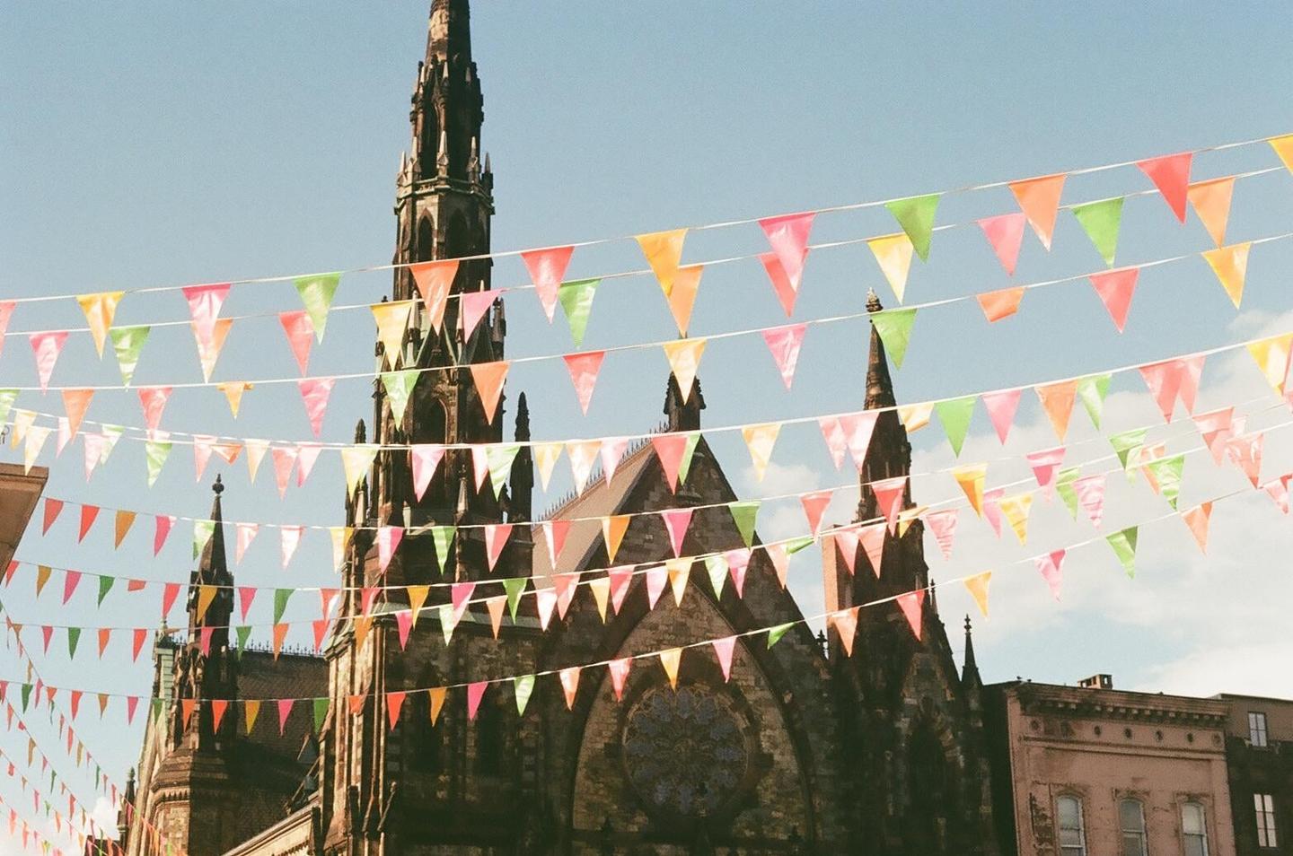 Colorful bunting hangs above a gothic church with a tall spire against a clear sky.