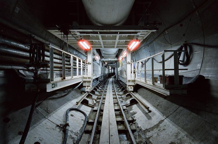 A long tunnel with train tracks in the center is illuminated by red lights.