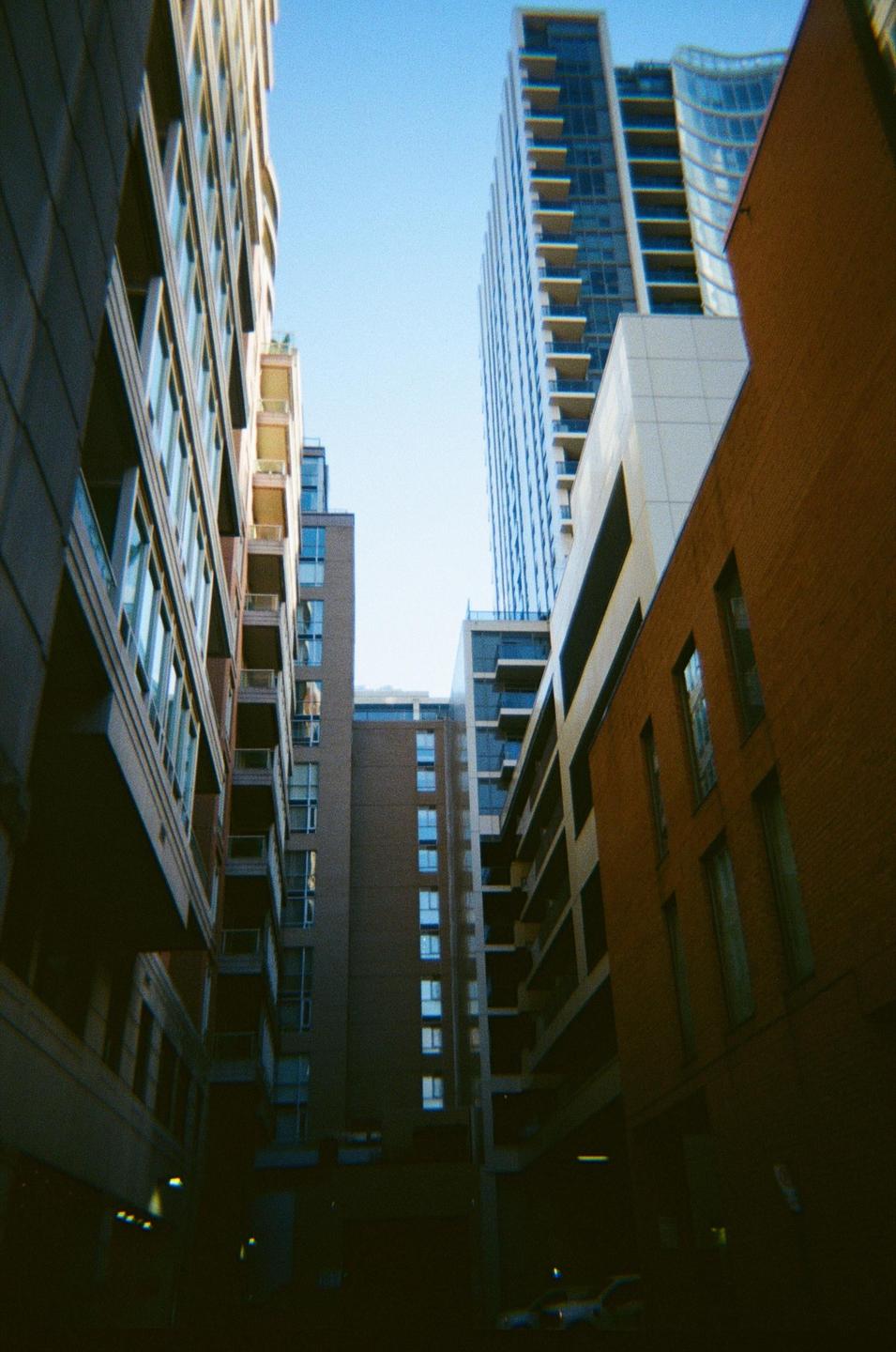 A low-angle view shows tall buildings with many windows and balconies, with a bright blue sky above.