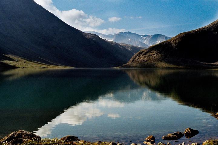 A large lake reflects the sky and surrounding mountains, with some snow visible on distant peaks.