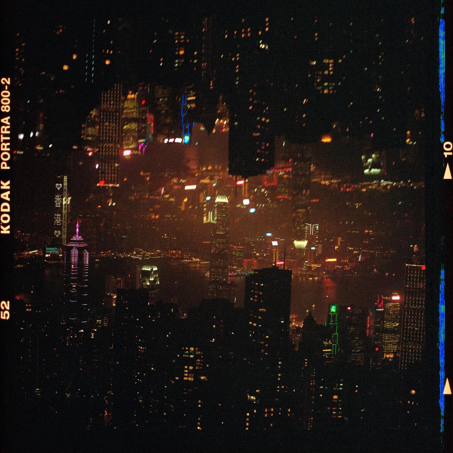A dark cityscape at night is illuminated by numerous lights from buildings and reflections on a body of water.