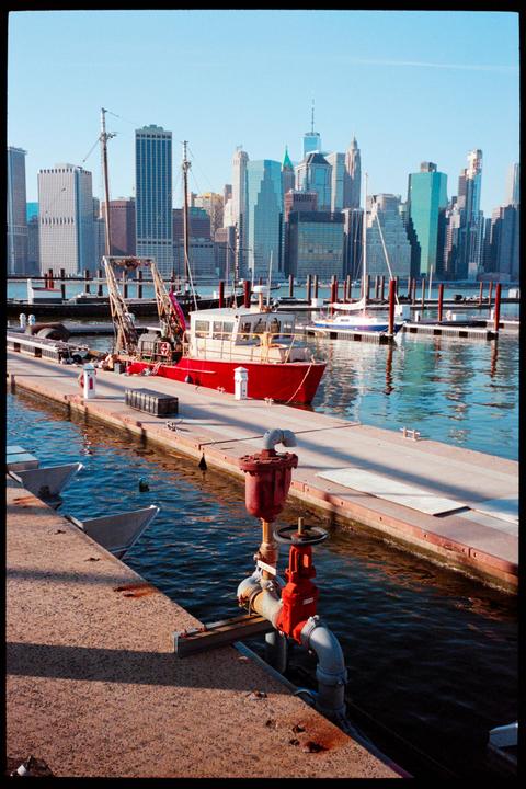 A red boat is docked at a pier with a city skyline in the background.
