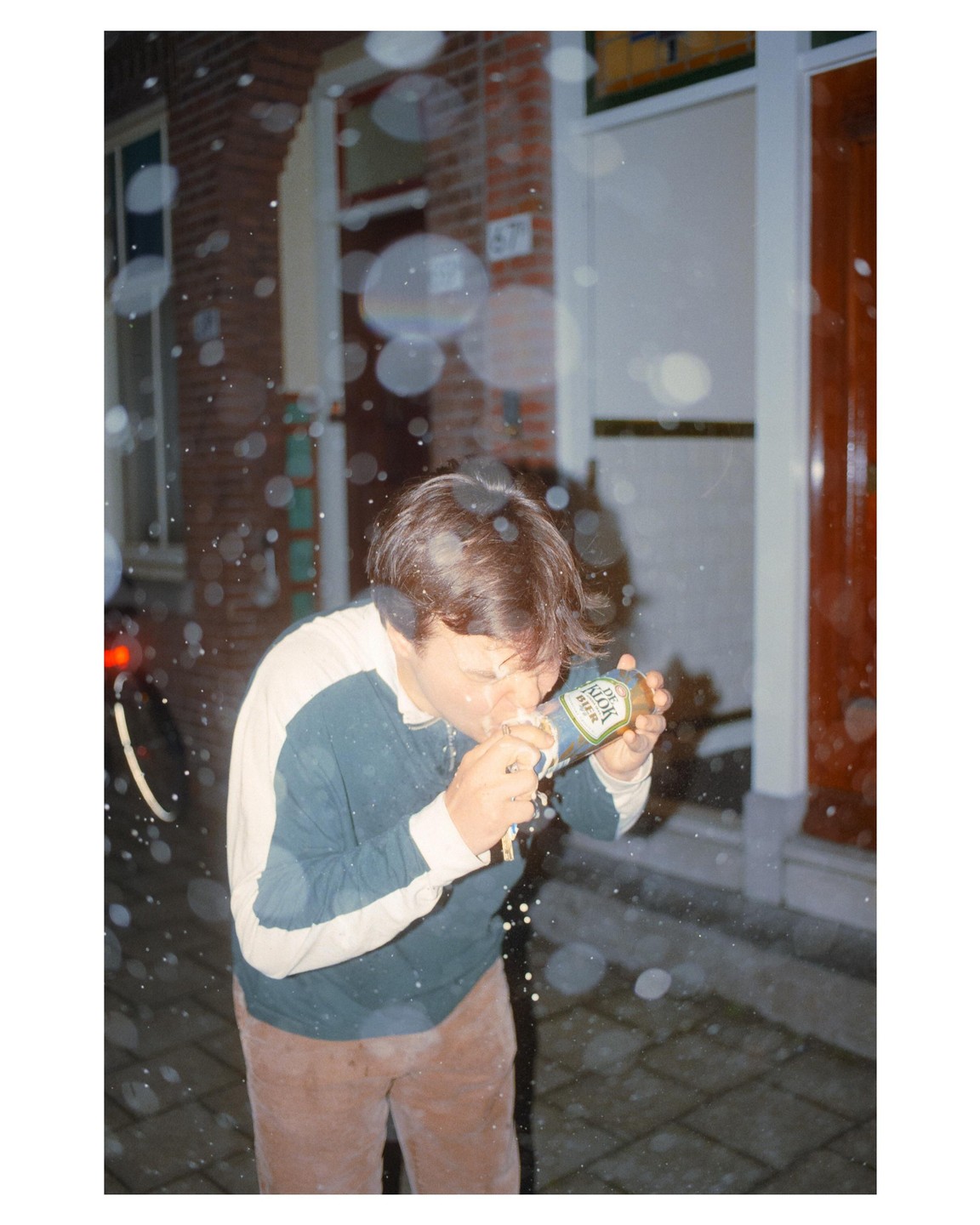 A man is showered with beer from a bottle on a street at night.