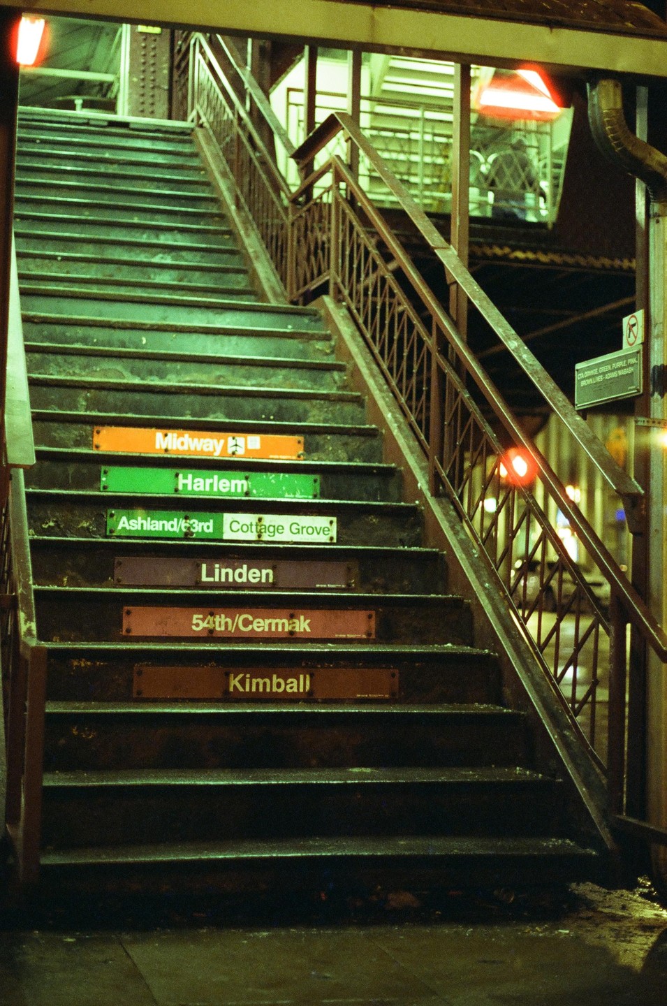 A long staircase with metal railings leads up to a subway platform with station names on the risers.