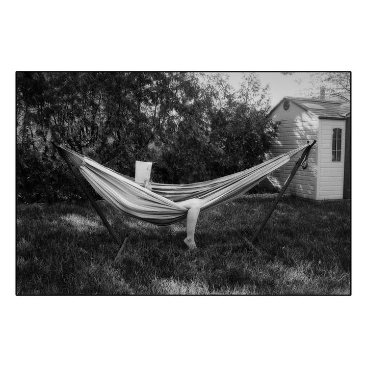A person is relaxing in a hammock in a grassy yard with a book.