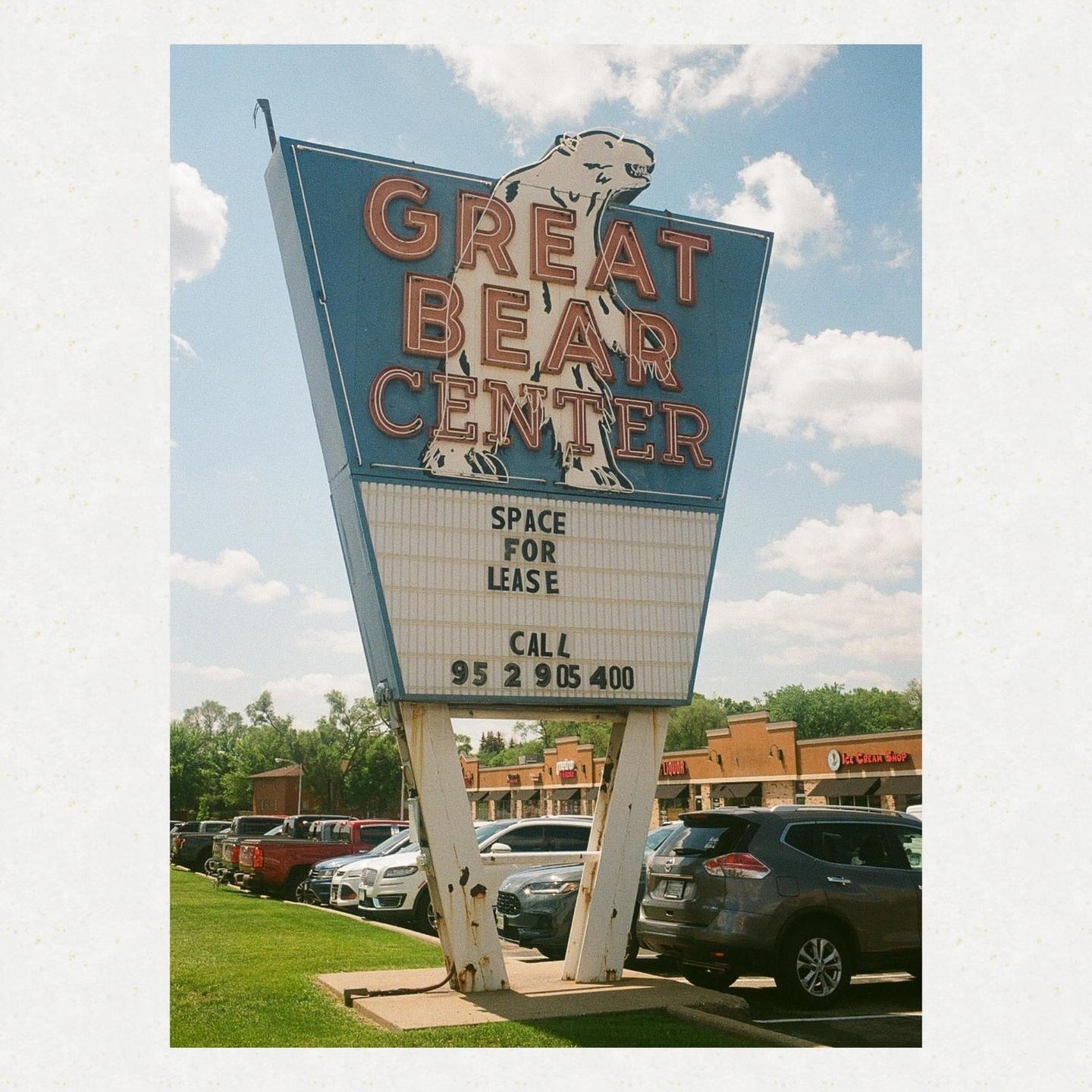 A large sign for the Great Bear Center with a polar bear illustration stands in a parking lot under a blue sky with clouds.