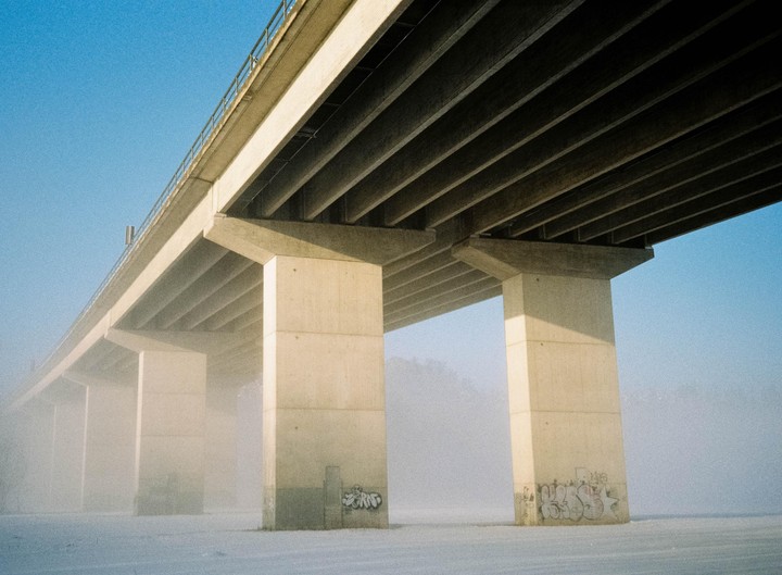A concrete highway bridge extends over a snow-covered landscape, partially obscured by fog.