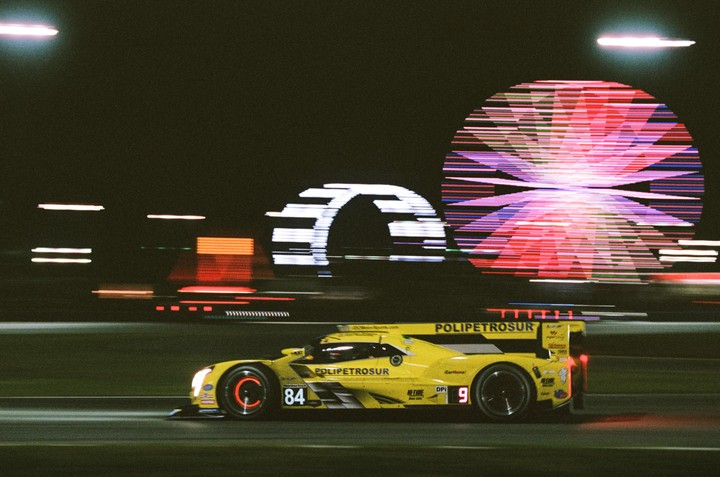 A yellow race car speeds past blurred lights at night.