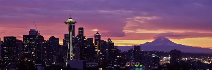 A panoramic view of the Seattle skyline at sunrise features the Space Needle and Mount Rainier in the distance.