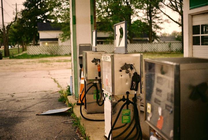 A row of old gas pumps with hoses and nozzles are visible at an abandoned service station.