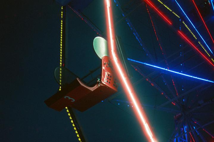 A red Ferris wheel gondola is illuminated by neon lights at night.