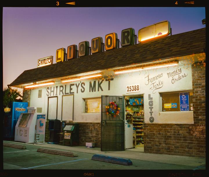A liquor store with a lit-up sign and Christmas lights is shown at dusk.