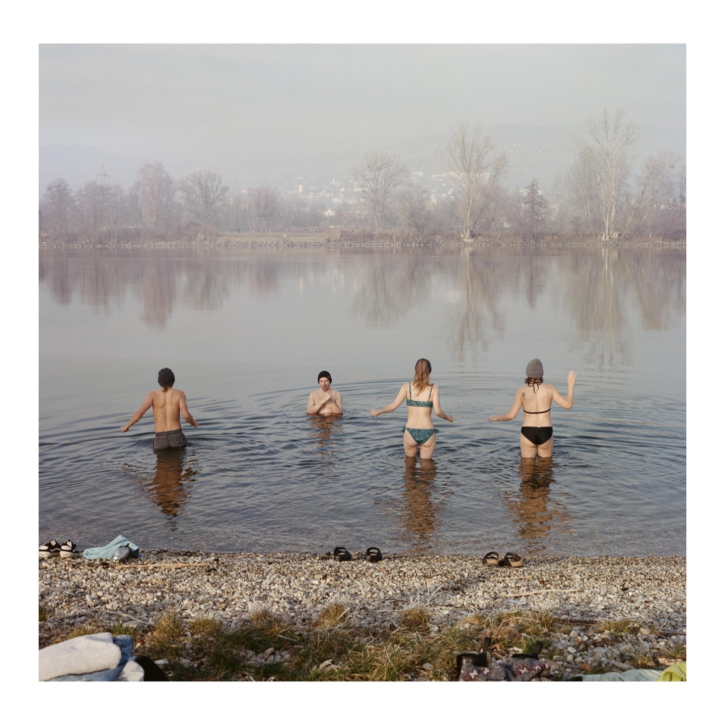 Two men and two women are standing in a river on a hazy winter day.