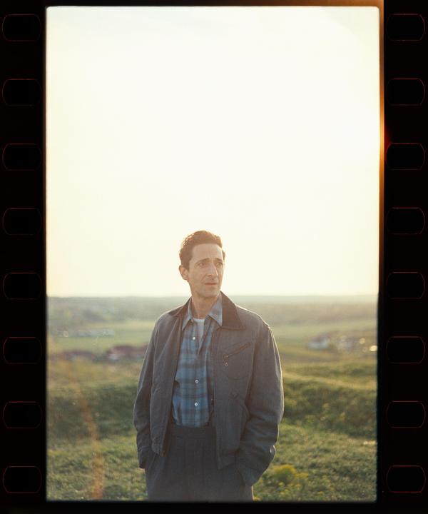 A man stands in a field at sunset, looking towards the right.