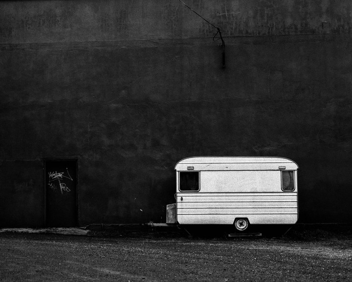 A white trailer is parked next to a dark wall with a door on the left.