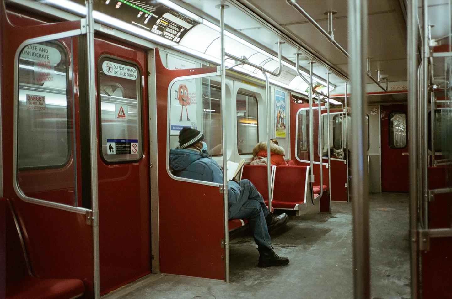 A man in a blue jacket and a woman in a red jacket sit on a subway train.