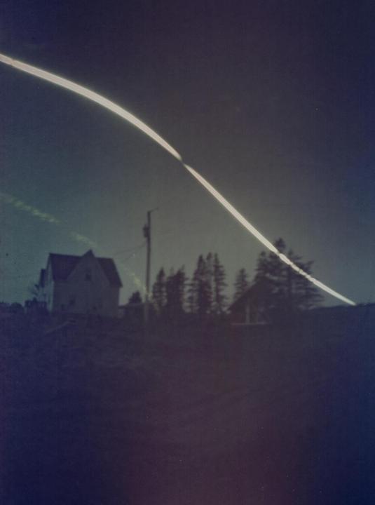 A long exposure photograph captures the sun's path across the sky above a house and trees.