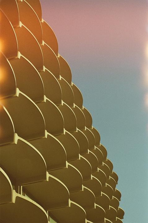 A building with a scaly facade is shown against a blue and pink sky.
