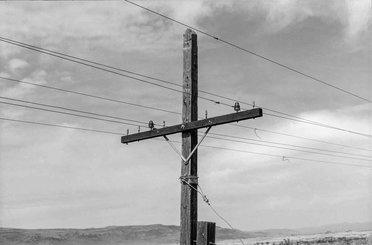 A wooden utility pole with multiple wires and insulators stands against a cloudy sky.