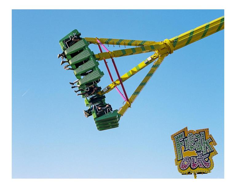People are riding a carnival swing ride against a clear blue sky, with a "Freak Out" sign visible in the lower right.