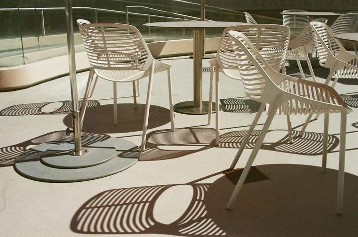 White chairs and tables cast striped shadows on a patio.
