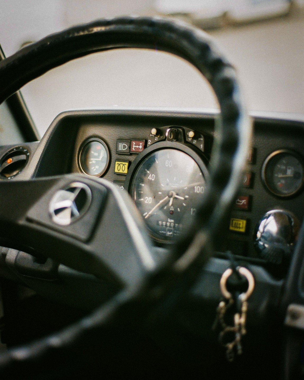 A steering wheel and dashboard with gauges and keys are visible inside a vehicle.