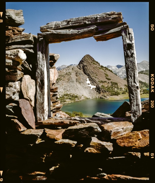 A mountain lake is visible through a window frame made of wood and stone.