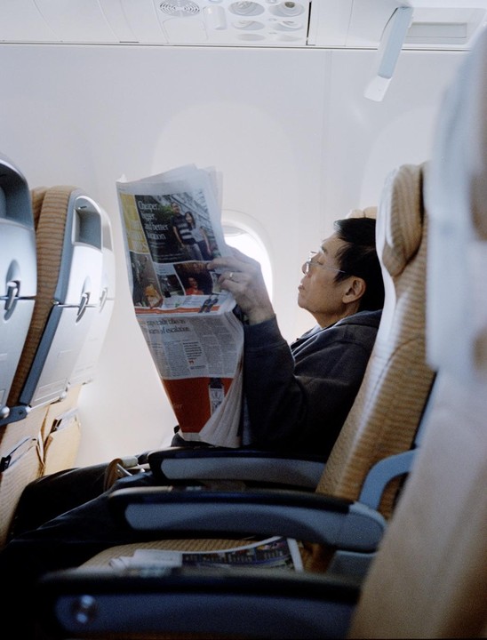 A man wearing glasses reads a newspaper while sitting in an airplane.