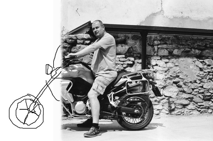 A man sits on a motorcycle in front of a stone wall.